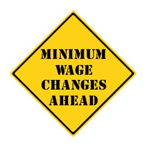 A yellow and black diamond shaped road sign with the words MINIMUM WAGE CHANGES AHEAD making a great concept.